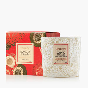 A Voluspa Tomato Trellis scented candle in a textured cream-ceramic glass jar, shown next to its red and green patterned retail box on a clean white background.