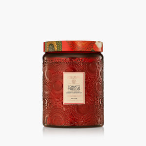 A red textured 18 oz glass jar candle with a patterned lid and a cream label reading Voluspa TOMATO TRELLIS' on a light gray background.