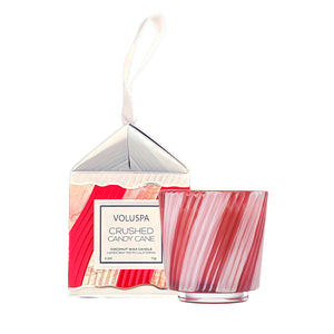 Voluspa Crushed Candy Cane coconut wax candle in a clear glass jar with red and white candy cane swirls, shown next to its patterned packaging box with a white hanging ribbon.