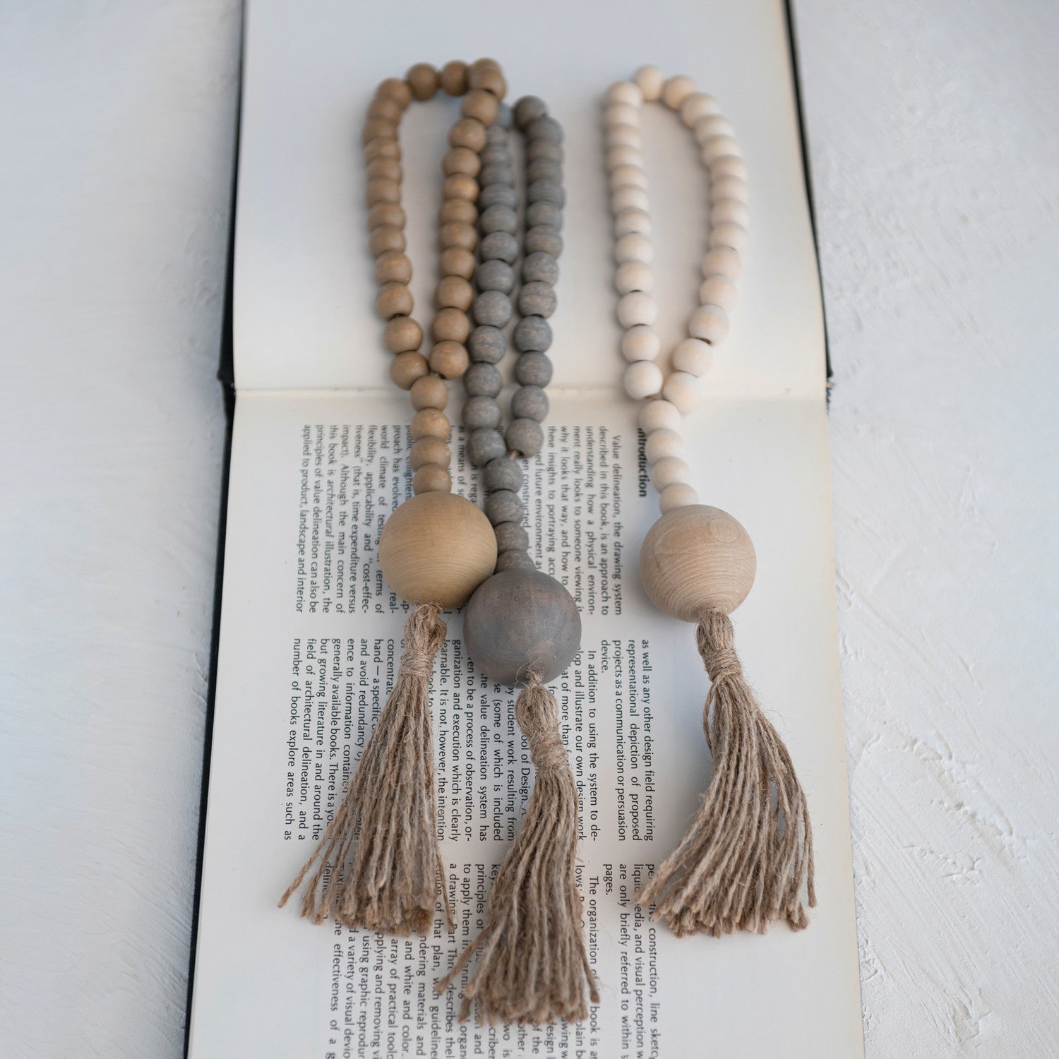 Three wooden beaded garlands with tassels on an open book in tan, blue, and cream colors. 