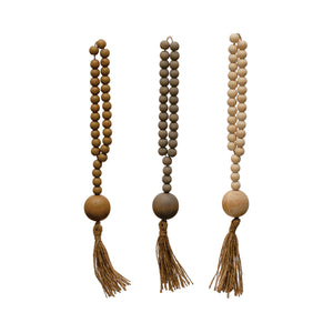 Three wooden beaded garlands with tassels on a white background. Tan, grey blue, and cream.