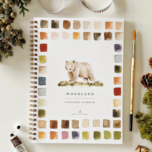 Woodland watercolor workbook with a bear illustration on a white surface with decorative woodland elements. Emily Lex Studios. 