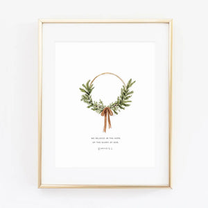 Framed watercolor artwork with a green wreath and brown ribbon bow and scriptural text against a white background. Emily Lex Studios. 