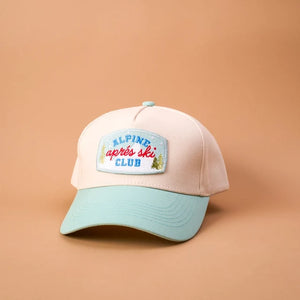 A pastel baseball cap with a light pink crown and a mint green brim, featuring a front patch that reads 'ALPINE apres ski CLUB'. The cap is photographed on a solid peach-colored background.
