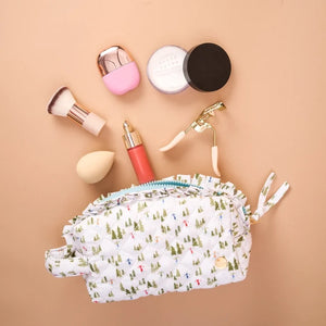 Makeup items including a brush, bottle, and compact on a beige background with a patterned pouch.