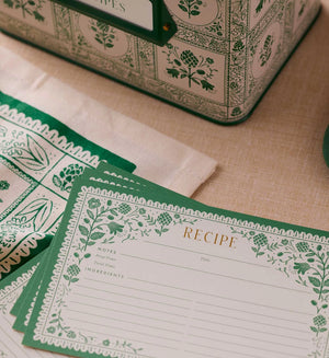 Set of 12 recipe cards with green floral artichoke design on a beige surface with matching recipe tin. 