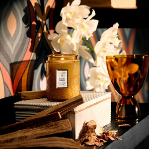 Decorative display with Baltic Amber candle, books, and white orchid flowers on a textured console table. Voluspa. 