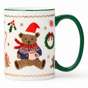 A white ceramic Christmas mug with a dark green handle and rim, decorated with a teddy bear wearing a red Santa hat and multicolor sweater, surrounded by holiday motifs like a wreath, candy cane, and gingerbread man.