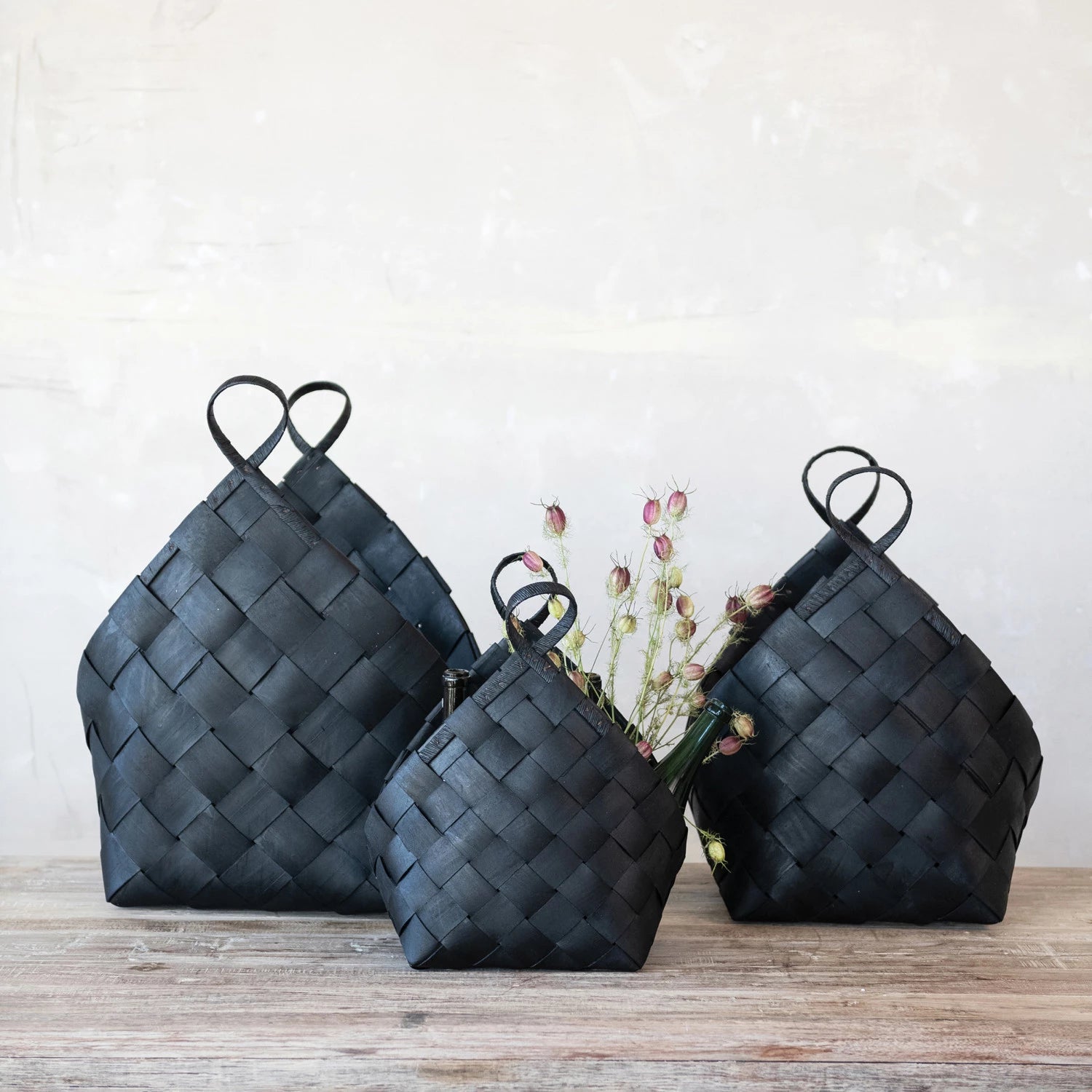 Set of three woven black wood baskets with handles on a wooden surface against white background. 