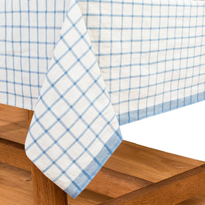 Blue and white checkered tablecloth draped over a wooden surface. French tablecloths. Couleur Nature. 