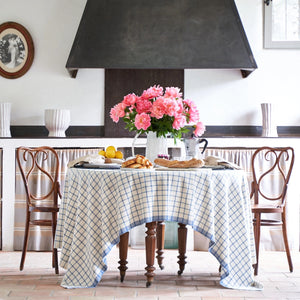 Kitchen table set with a checkered tablecloth, flowers, and bread, with a black range hood above.