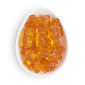 A pile of translucent orange gummy bear candies arranged in a white oval dish on a clean white background.