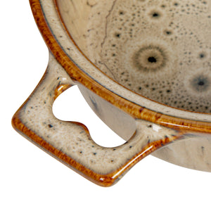 Close-up of a ceramic brie maker with speckled glaze and brown rim on a white background. 