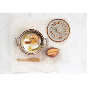 Ceramic artisan brie baker dish with brie cheese and pears displayed inside on a marble surface.