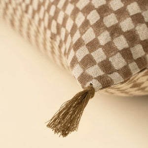 Checkered brown pillow with brown tassel on a beige background. 