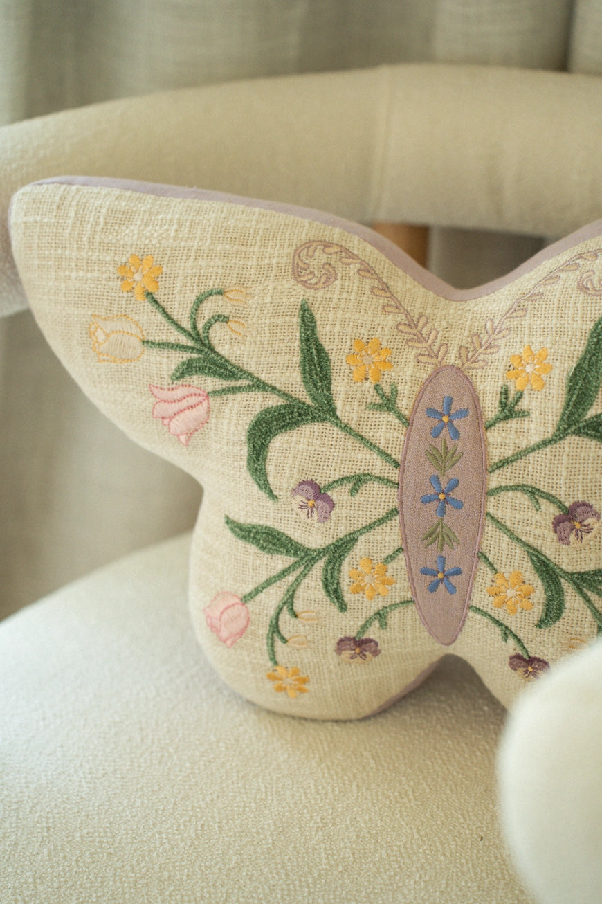 Butterfly-shaped pillow with floral embroidery on a beige chair.