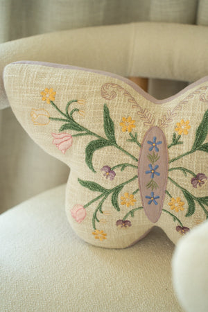 Butterfly-shaped pillow with floral embroidery on a beige chair.
