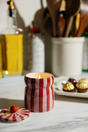 Striped candle in a kitchen setting with utensils and a bottle in the background