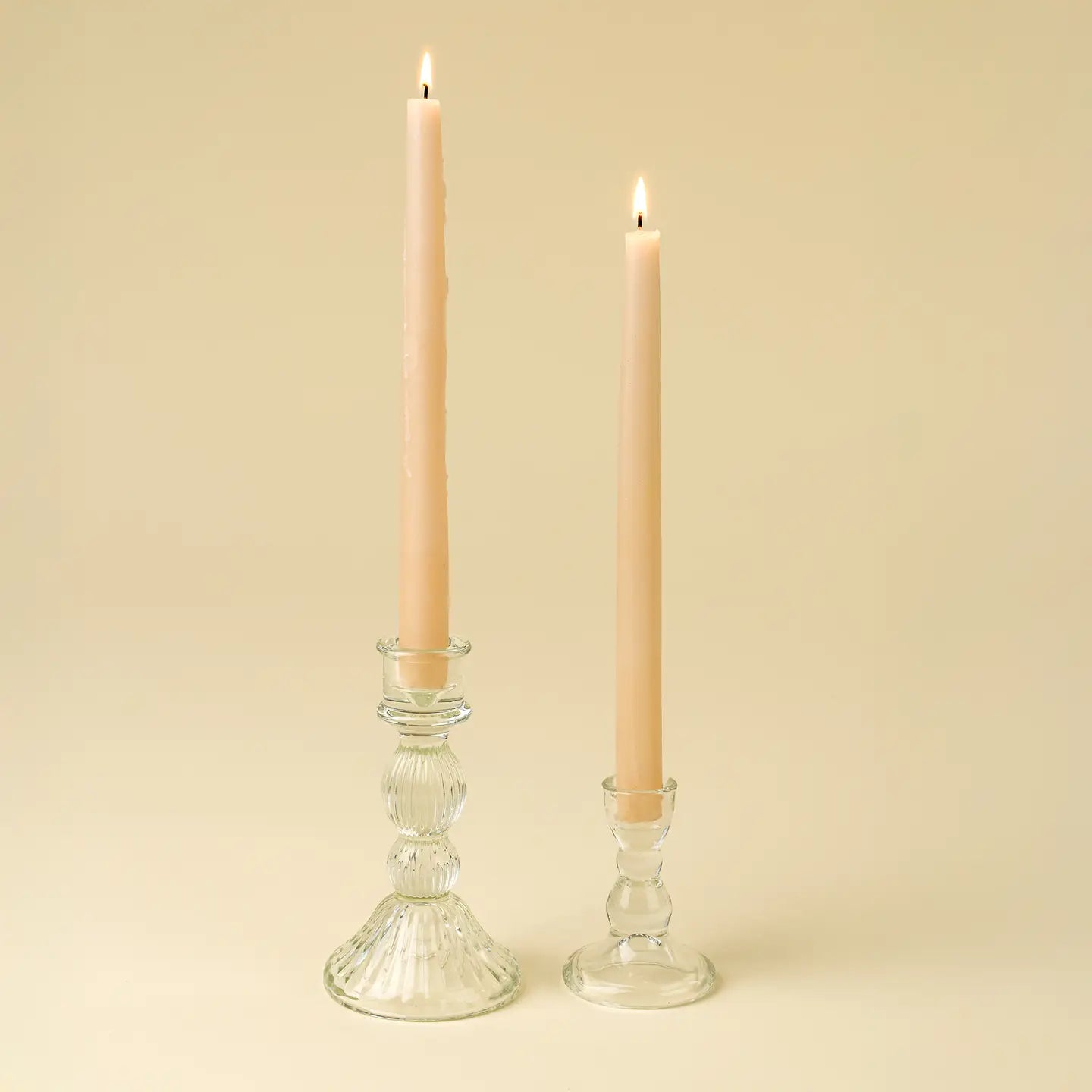 Two glass candle holders with lit candles on a beige background