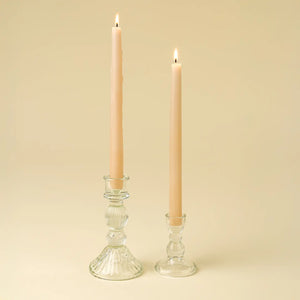 Two glass candle holders with lit candles on a beige background