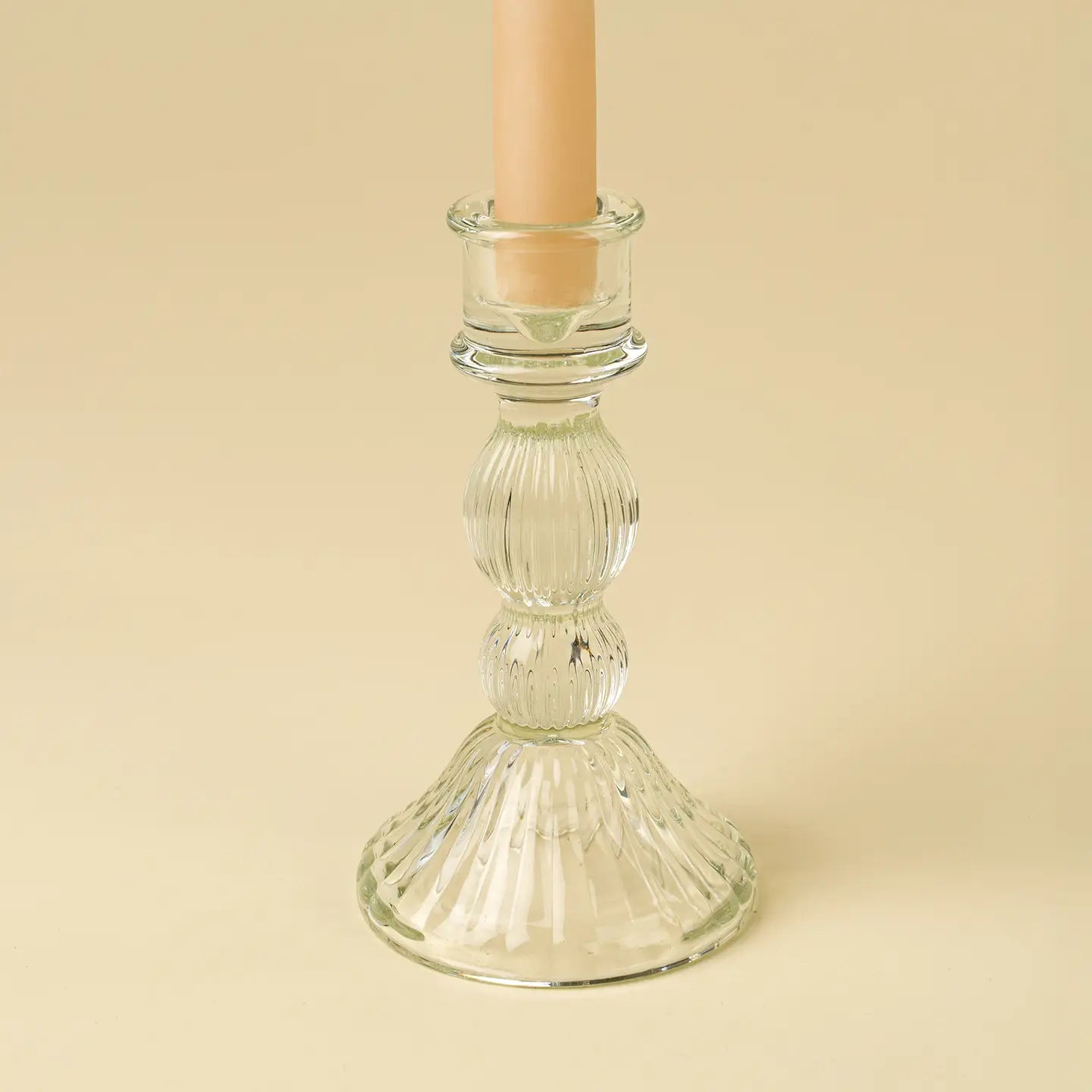 Clear glass candle holder with a beige candle on a beige background