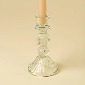 Clear glass candle holder with a beige candle on a beige background
