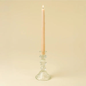 Clear glass candle holder with a lit pink candle on a beige background