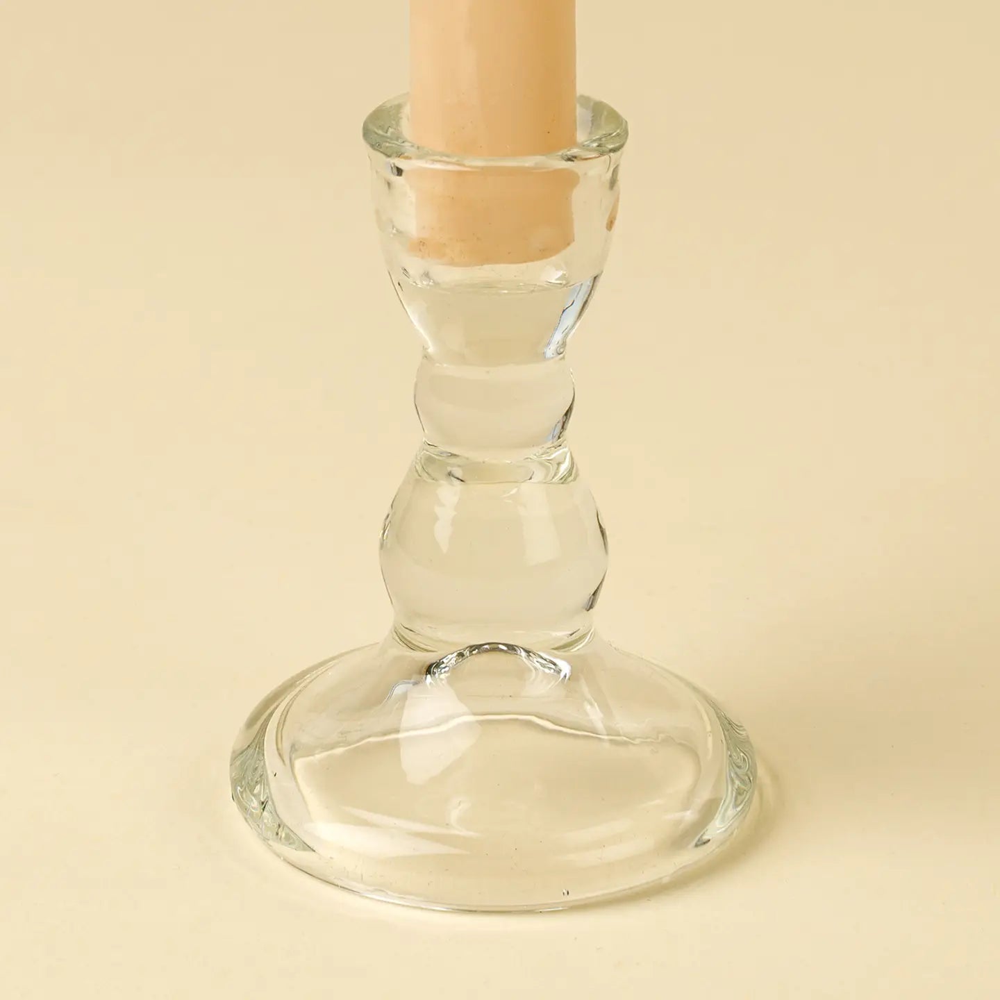 Clear glass candle holder with a beige candle on a beige background