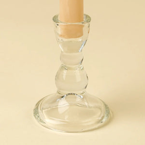 Clear glass candle holder with a beige candle on a beige background