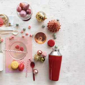 Decorative holiday table setting with a red martini shaker, candy canes stir sticks, and Christmas ornaments on a light surface.
