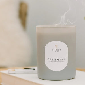 Candle labeled 'Cashmere' by LINNEA on a table with a blurred background