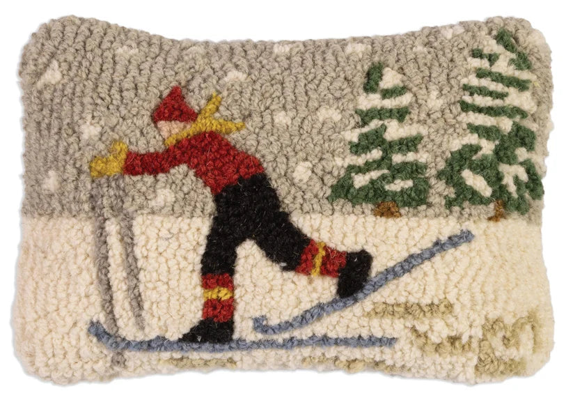 A rectangular hand-tufted rug featuring a winter scene with a skier in a red jacket and black pants, set against a snowy background with pine trees.
