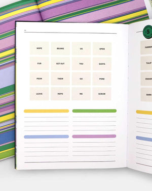 An open puzzle book showing printed pages with words in a grid and colored highlight lines, photographed on a striped multicolor background.