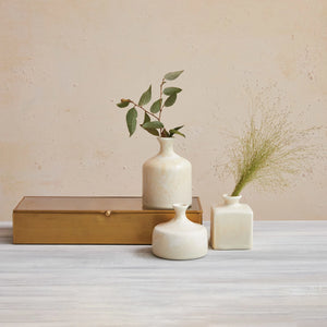 Three coordinating stoneware vases filled with plant stems on a gold metal box against a beige wall.