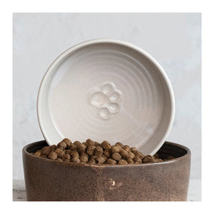 Individual ceramic debossed paw print dog bowl placed inside another dark brown ceramic dog bowl filled with dry kibble. 