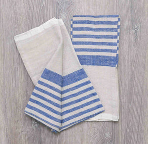 Two folded linen and cotton hand towels with denim blue and natural stripes on a wooden table surface. 