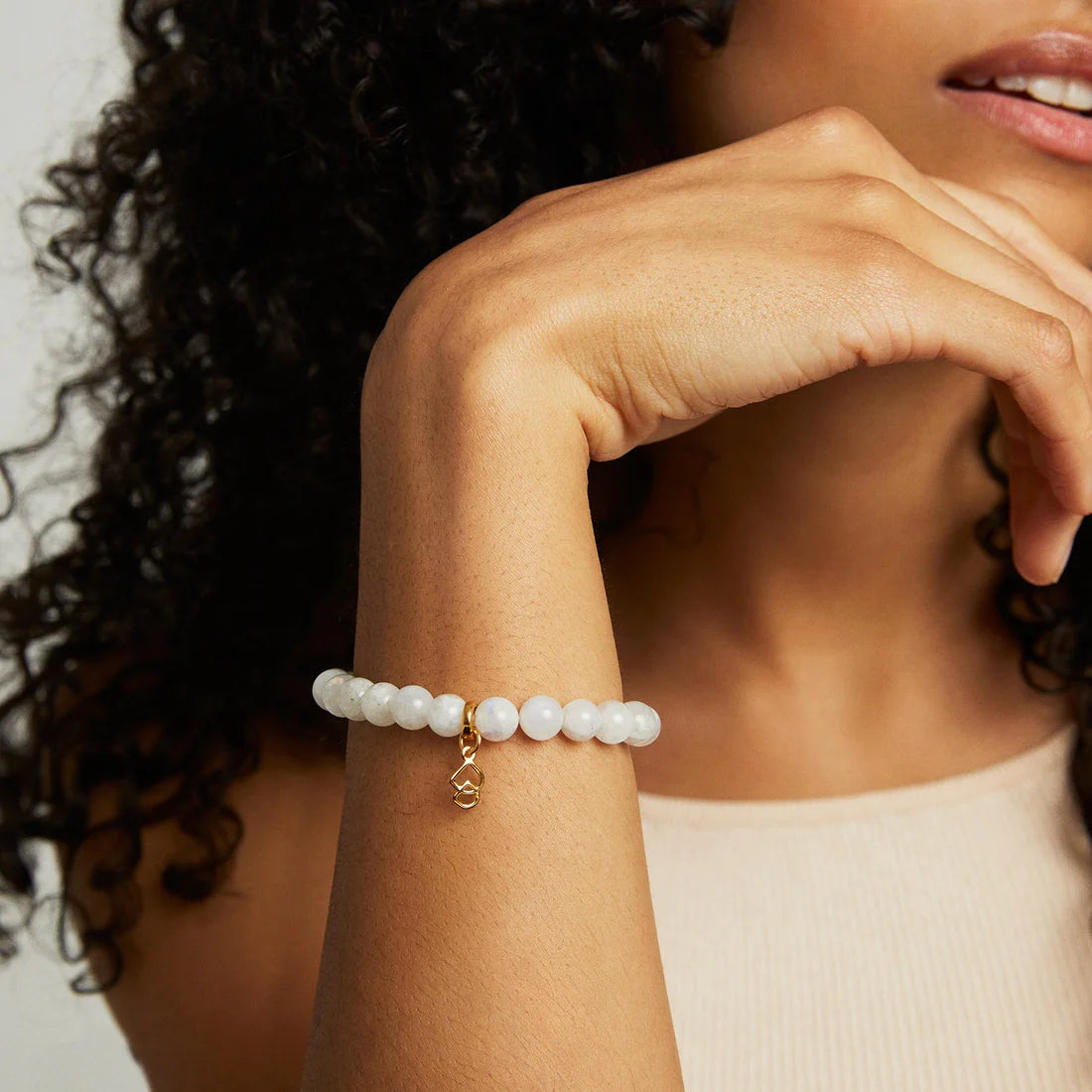 Woman wearing a beaded Moonstone bracelet with a gold charm on a neutral background. Dean Davidson jewelry.