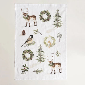 A white cotton tea towel with Christmas greenery illustrations, including trees and a reindeer, Christmas wreaths, holly, pinecones, and a bird. Emily Lex Studio. 