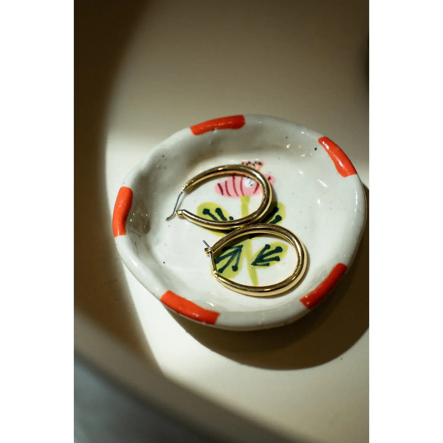 Gold set of hoop earrings on a hand painted flora inspired stoneware dish with multicolored accents.