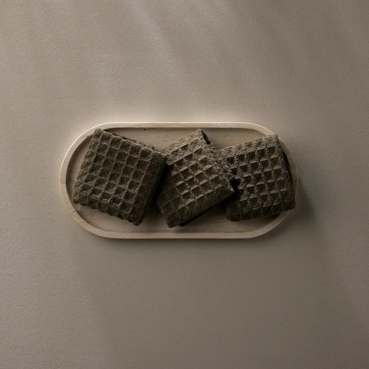Three dark waffle weave washcloths on a beige plate against a matching background