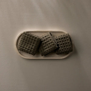 Three dark waffle weave washcloths on a beige plate against a matching background