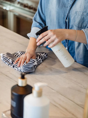 Person cleaning a surface with Geometry cloth and L'AVANT bottle of cleaning solution in a kitchen setting.
