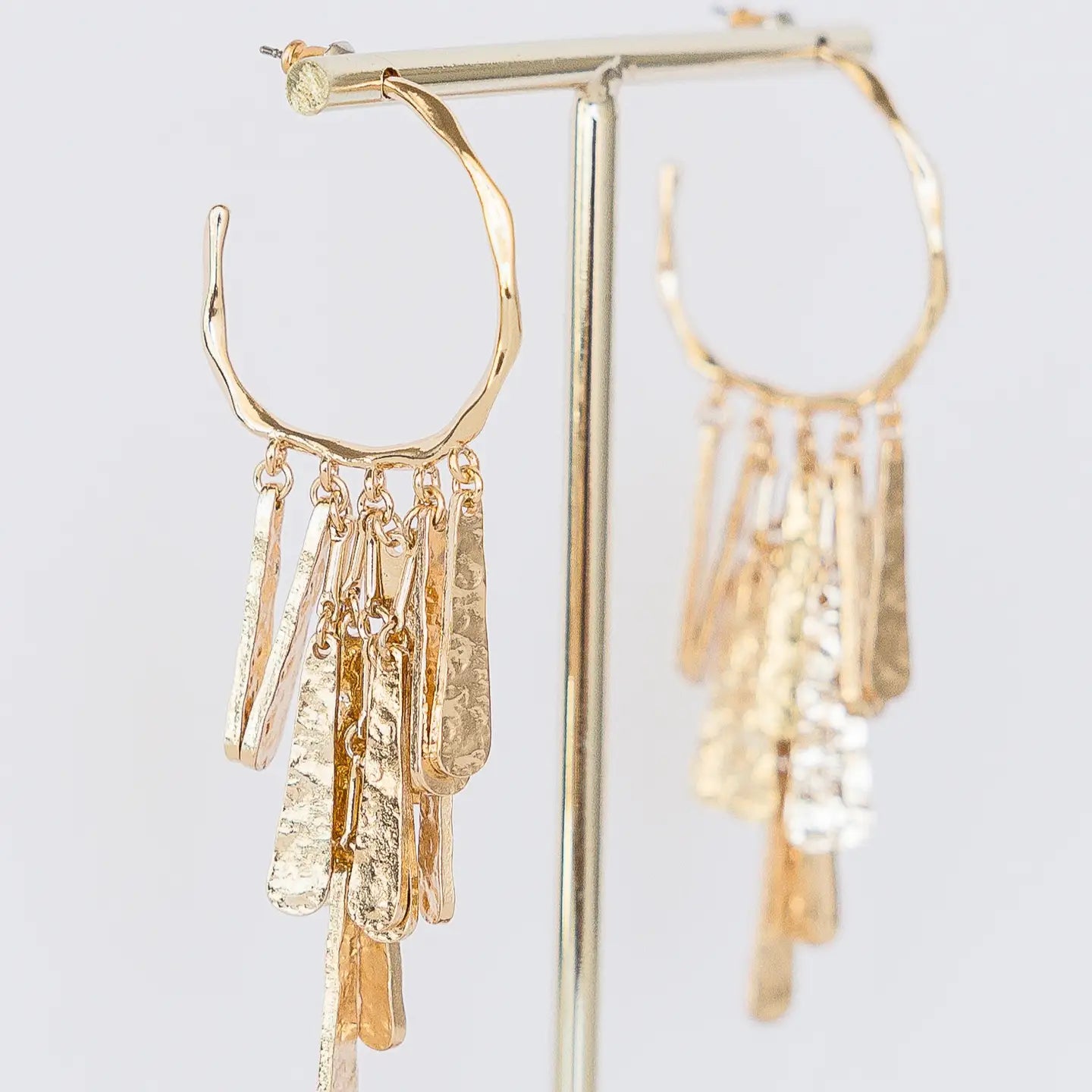 Hammered texture gold dangle bar earrings displayed on gold earring stand. Made in the USA