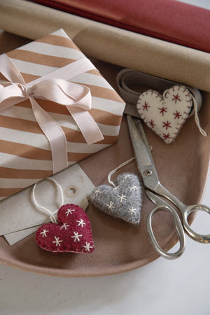 Gift box with striped paper, heart-shaped decorations, and scissors on a wooden surface.