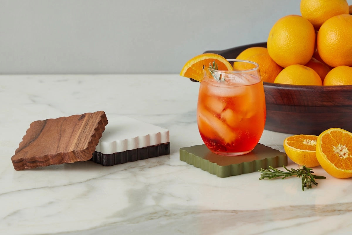 Set of four heritage wood coasters. Brown, White, Dark Walnut, and Sage Green displayed with cocktail. 