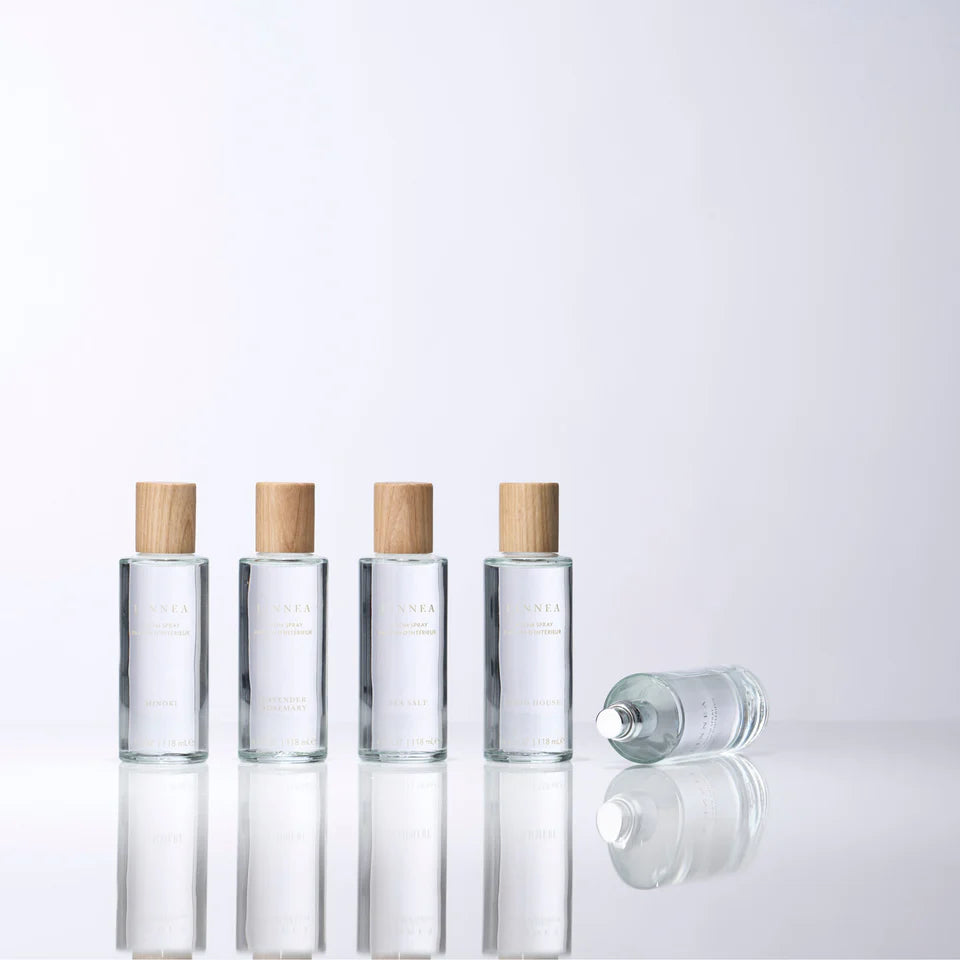 Set of five room and body sprays in a clear glass bottle with wooden caps against a light gray background. Linnea and Co. 