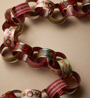 A decorative paper chain garland made of patterned paper loops in holiday colors, including red, green, pink, white, and gold, arranged on a neutral beige background.