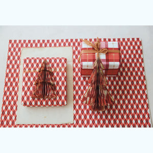 Two wrapped gift boxes with decorative paper tree ornaments, arranged on a red-and-white holiday plaid patterned sheet of wrapping paper with a cream card underneath, on a light neutral background.