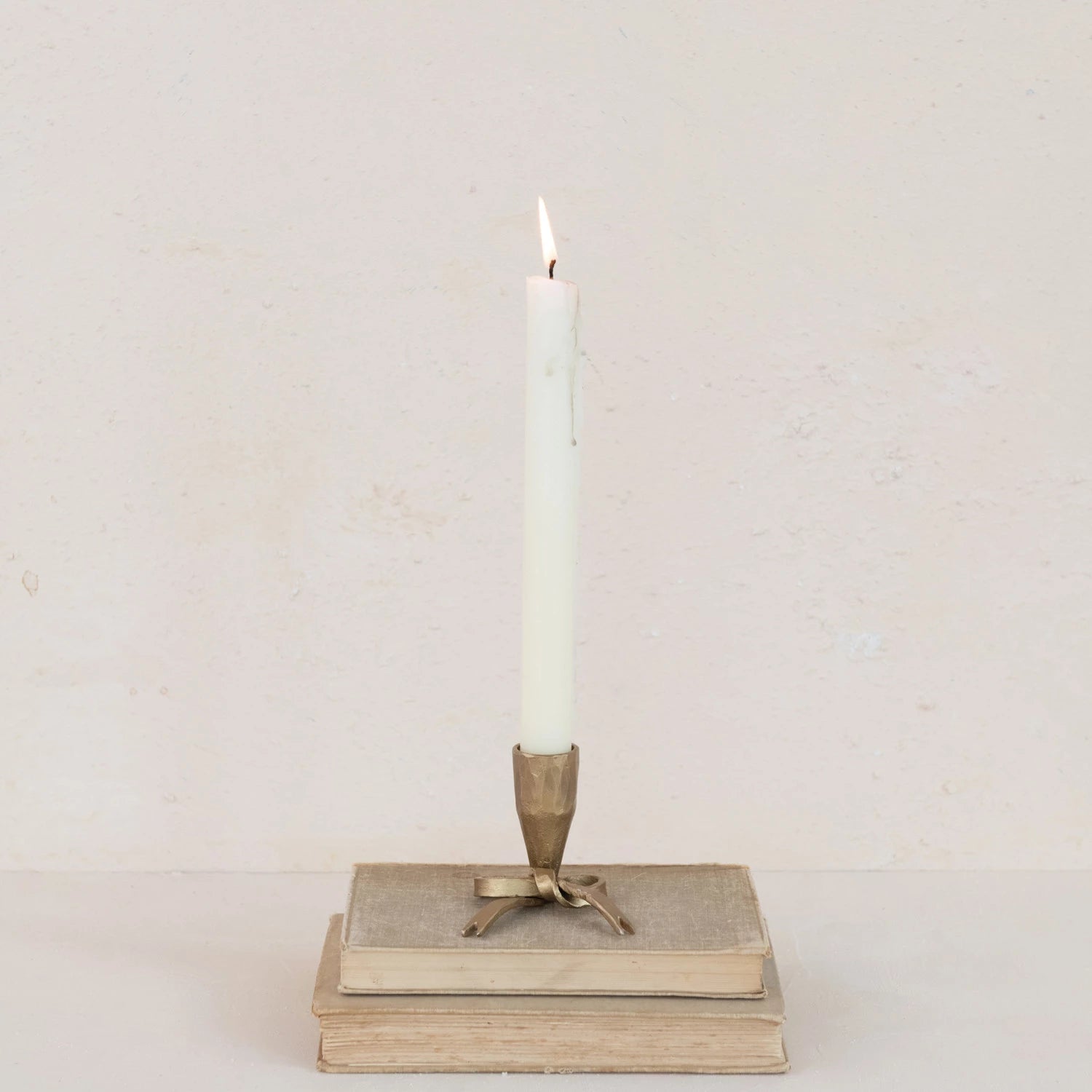 Decorative iron bow taper holder with mini candle on top of stacked books against a plain background. 