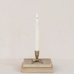Decorative iron bow taper holder with mini candle on top of stacked books against a plain background. 